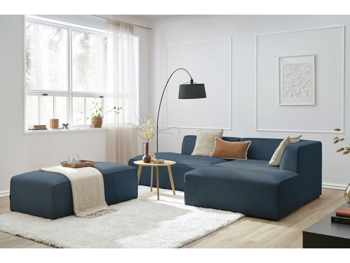 Kampinė modulinė sofa su pufu, tamsiai mėlyna šalia kavos staliuko